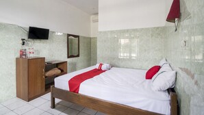 Habitación de hotel con cama de madera, colcha roja y blanca, armario de madera, televisor montado en la pared y lámpara de pared roja.