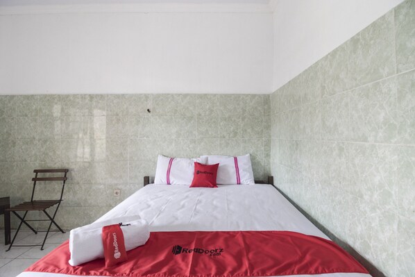 A hotel room with a bed, a chair, and a tiled wall. - RedDoorz @ Sagan Jogja 2 (Yogyakarta)