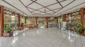 Un espacio interior amplio con suelo de baldosas, una zona de estar central con mesas y sillas, y una barra con diversos artículos.