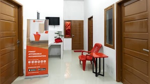 A hallway with wooden doors, a red chair, a small table, and a RedDoorz advertisement. - RedDoorz @ Jalan Dr Mansyur Medan 2 (Medan)