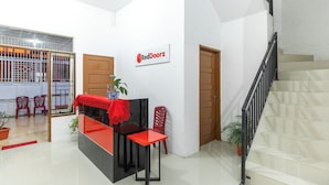 A reception area with a red and black desk, a potted plant, and a staircase. - RedDoorz @ Jalan Dr Mansyur Medan 2 (Medan)