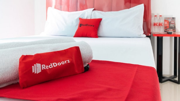 A hotel room with a red and white bedspread, a red pillow with the RedDoorz logo, and a neatly made bed. - RedDoorz @ Jalan Dr Mansyur Medan 2 (Medan)