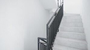 Uma escadaria com guarda-corrimão de metal preto e degraus brancos.