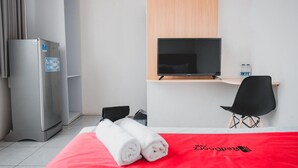 Quarto de hotel com cama, televisão, escrivaninha, cadeira e frigorífico.