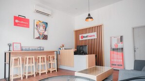 Um saguão de hotel moderno com balcão de recepção, banquetas de madeira, uma mesa de vidro e a marca RedDoorz.