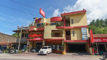 A two-story building with a red and yellow facade, a sign for 'Hotel Sedayu 1', and a parked white car in front.