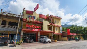 A hotel named RedDoorz with a red and yellow facade, a balcony, and a parked car in front.
