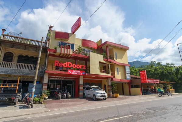 A hotel named RedDoorz with a red and yellow facade, a balcony, and a parked car in front.