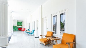 A hotel corridor with white walls, a green accent wall, and orange and blue chairs. - RedDoorz near Grojogan Sewu Tawangmangu (Tawangmangu)