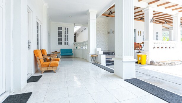 A spacious indoor area with a tiled floor, wooden chairs, a blue sofa, and a small table. - RedDoorz near Grojogan Sewu Tawangmangu (Tawangmangu)