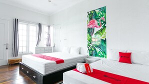 A hotel room with two beds, a large window with curtains, a tropical-themed wall painting, and a RedDoorz logo on the beds. - RedDoorz near Grojogan Sewu Tawangmangu (Tawangmangu)
