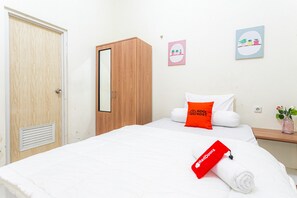 A hotel room with a wooden wardrobe, a bed with white bedding, a red pillow, and a RedDoorz towel.