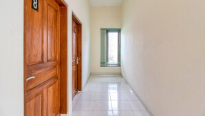 Un pasillo con puertas de madera, una ventana con persianas y suelo de baldosas.