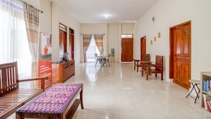 Un hall de hotel con una recepción, una zona de estar con una mesa y sillas, y una escalera que sube a otros pisos.