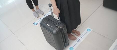 A person pulling a black suitcase with wheels, standing on a tiled floor with directional signs.