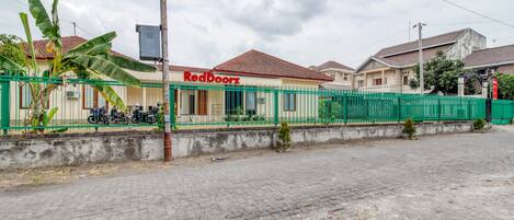 A building with a sign reading "RedDoorz" and a green fence in front.