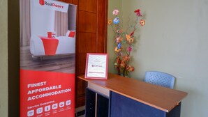 A reception desk with a RedDoorz sign, a framed certificate, and a floral arrangement.