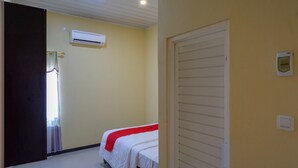 A hotel room with a bed, an air conditioning unit, a door, and a light switch on the wall.