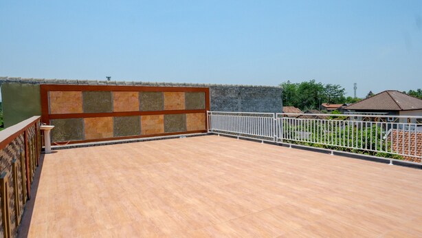 A rooftop terrace with a tiled floor, a metal railing, and a stone wall.
