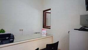 Ein kleines Büro mit einem Glastisch, einem Drucker, einem Spiegel und einem weißen Kühlschrank.