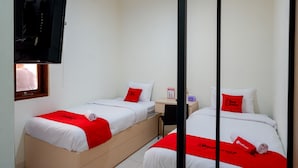 Ein Hotelzimmer mit zwei Betten, jeweils mit einer roten und weißen Bettdecke und passenden Kissen. Ein Fernseher ist an der Wand montiert und ein kleiner Tisch steht zwischen den Betten.