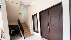 A staircase leading to a landing with a large wooden door and a small window with curtains. - KoolKost Syariah near Alun Alun Kota Bandung (Bandung)