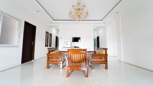 A spacious room with a dining table surrounded by wooden chairs, a chandelier, and a flat-screen TV on the wall. - KoolKost Syariah near Alun Alun Kota Bandung (Bandung)