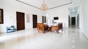 A spacious living area with a chandelier, a dining table with chairs, a TV mounted on the wall, and a hallway leading to other rooms. - KoolKost Syariah near Alun Alun Kota Bandung (Bandung)