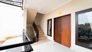 A clean, modern interior with a staircase leading to an upper floor, a wooden door, and a large window offering a view of the outside. - KoolKost Syariah near Alun Alun Kota Bandung (Bandung)