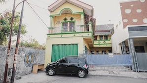 Una casa de dos pisos con una puerta de garaje verde, un balcón y un coche pequeño estacionado al frente.