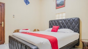Una cama bien hecha con una colcha roja y blanca, un cabecero negro y una mesita redonda al lado.