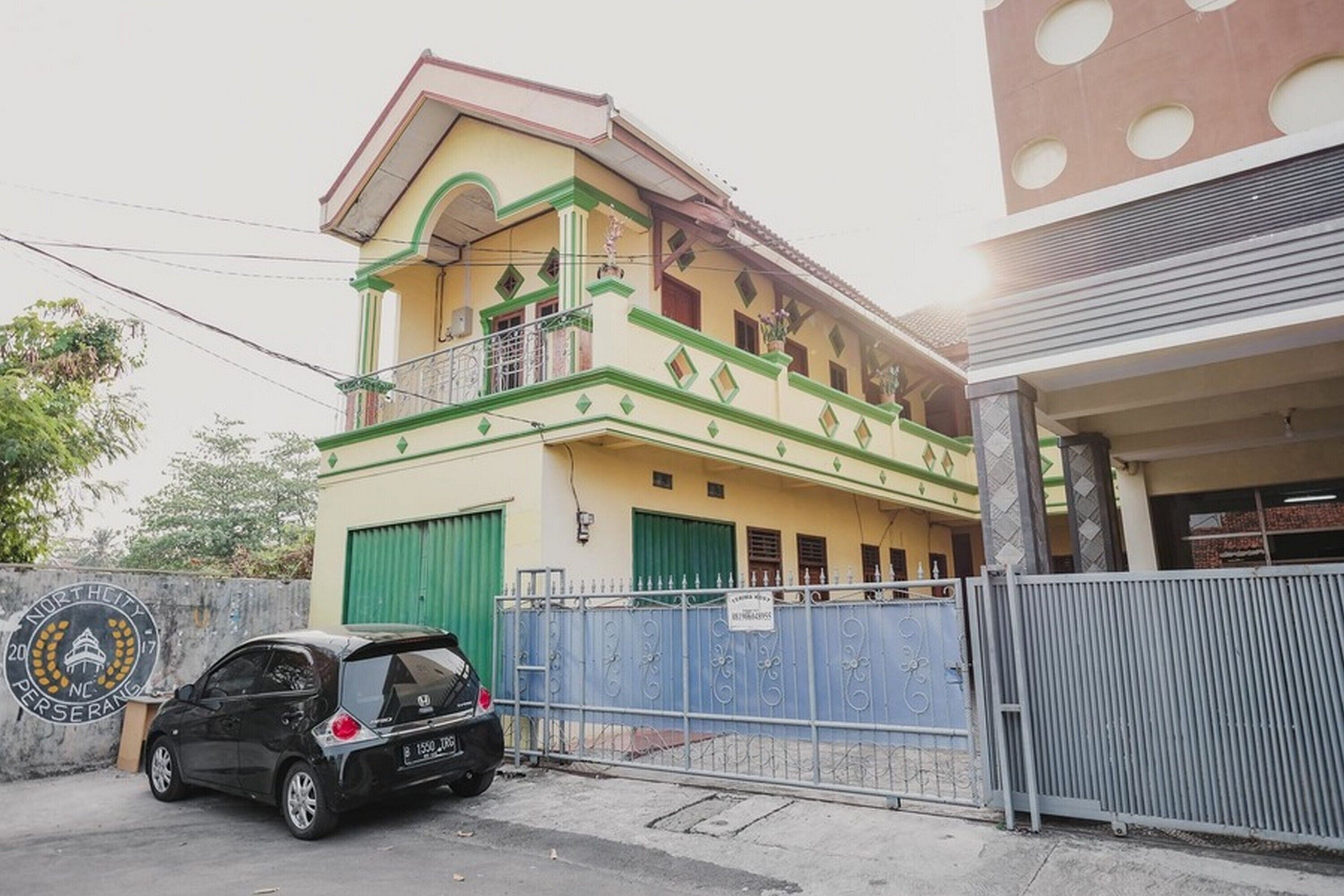 A two-story building with a balcony on the upper floor, a gated entrance, and a parked car in front.