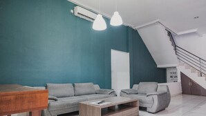 A modern living room with teal walls, a wooden coffee table, grey sofas, and a staircase. - RedDoorz @ Jalan Hayam Wuruk Lampung 2 (Bandar Lampung)