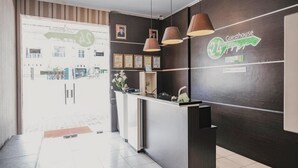 A hotel reception area with a modern design, featuring a reception desk, pendant lights, framed certificates, and a sign indicating a 24-hour guesthouse service. - RedDoorz @ Jalan Hayam Wuruk Lampung 2 (Bandar Lampung)