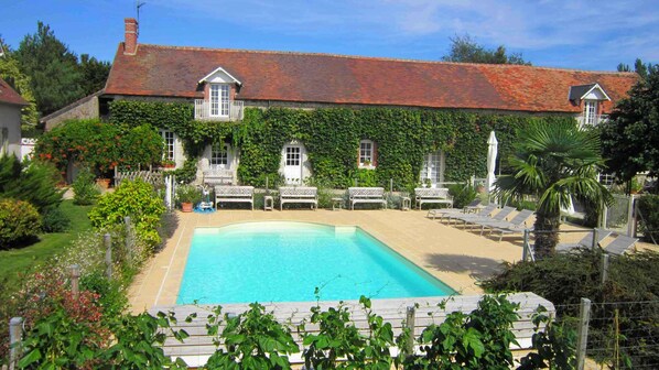 Une grande maison avec une piscine, entourée d’une végétation luxuriante et d’un jardin bien entretenu.