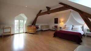 A spacious attic bedroom with a large bed, a crib, and a wooden dresser.