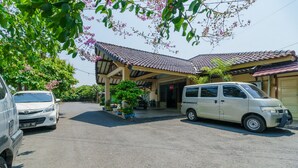 A parking area with a white van and a white car parked in front of a building with a tiled roof and covered entrance.