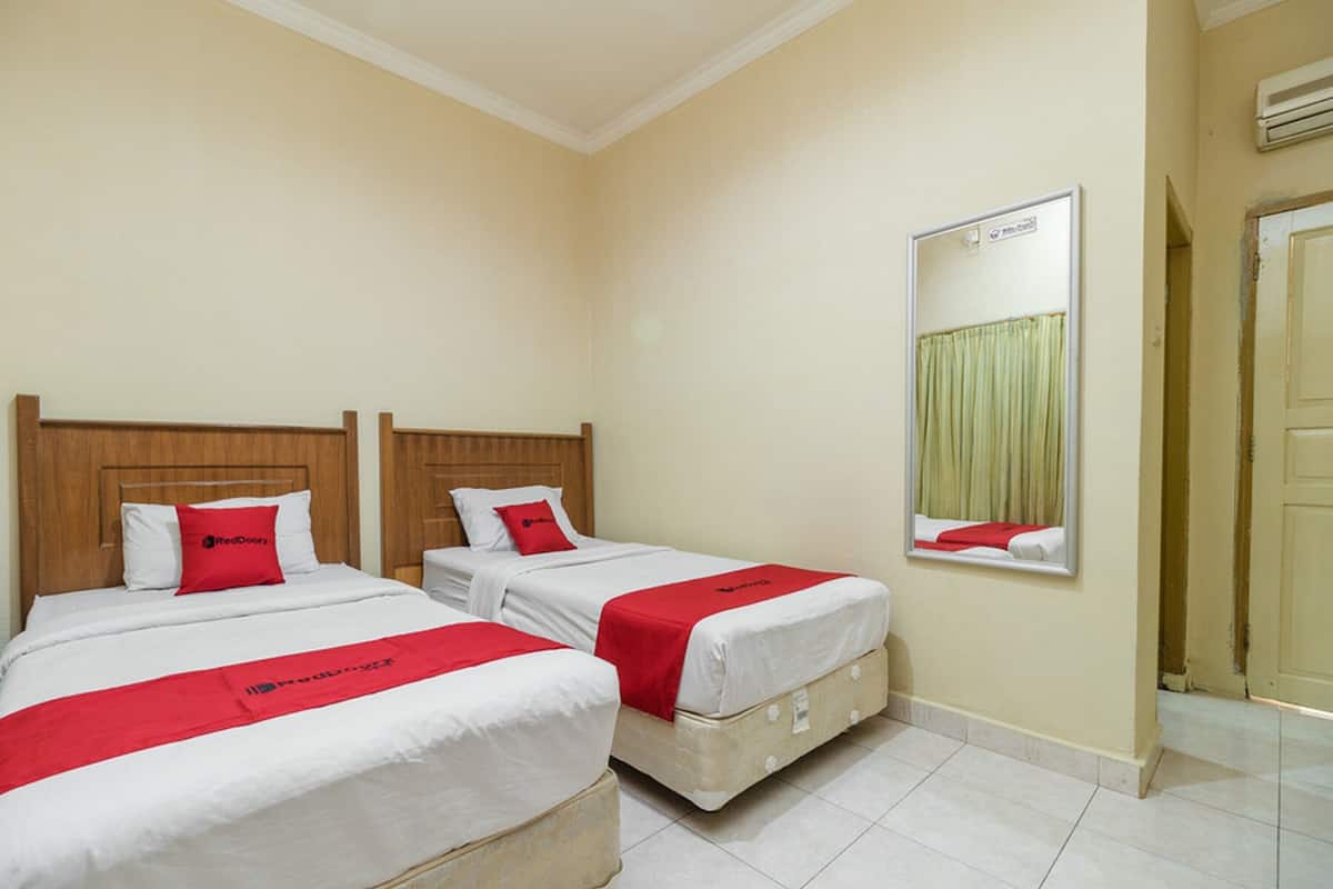 Een hotelkamer met twee bedden, elk voorzien van een houten hoofdbord, wit beddengoed en rode accenten.