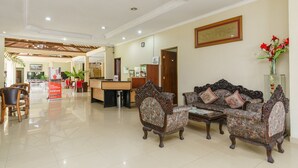 A hotel lobby with a reception desk, two ornate sofas, a coffee table, and a reception area with a counter and chairs.