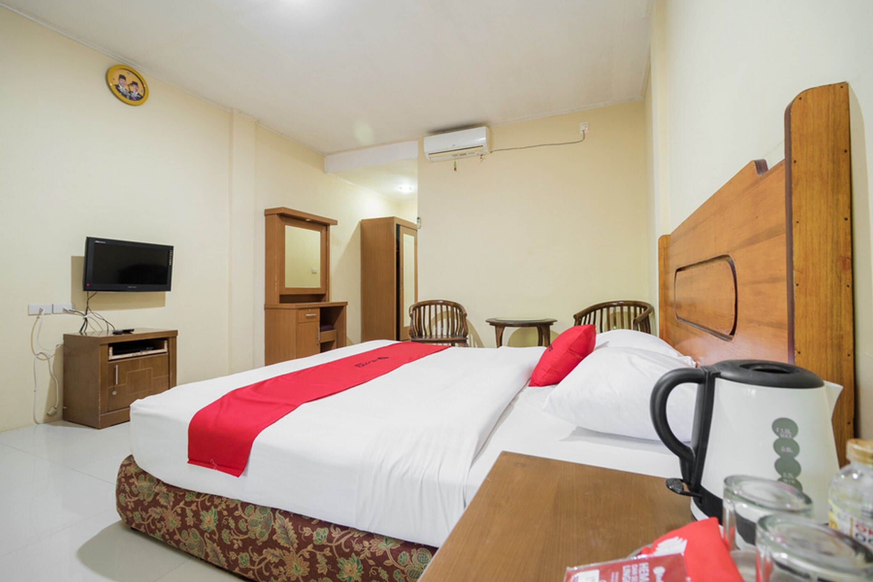 Ein Hotelzimmer mit einem Bett, einem Holz-Kopfteil, einem Fernseher, einem Kleiderschrank, einem Spiegel, einem kleinen Tisch und einem Wasserkocher.