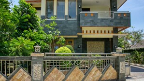 Una casa moderna de dos pisos con fachada de piedra, entrada protegida por una reja y un jardín cuidado.