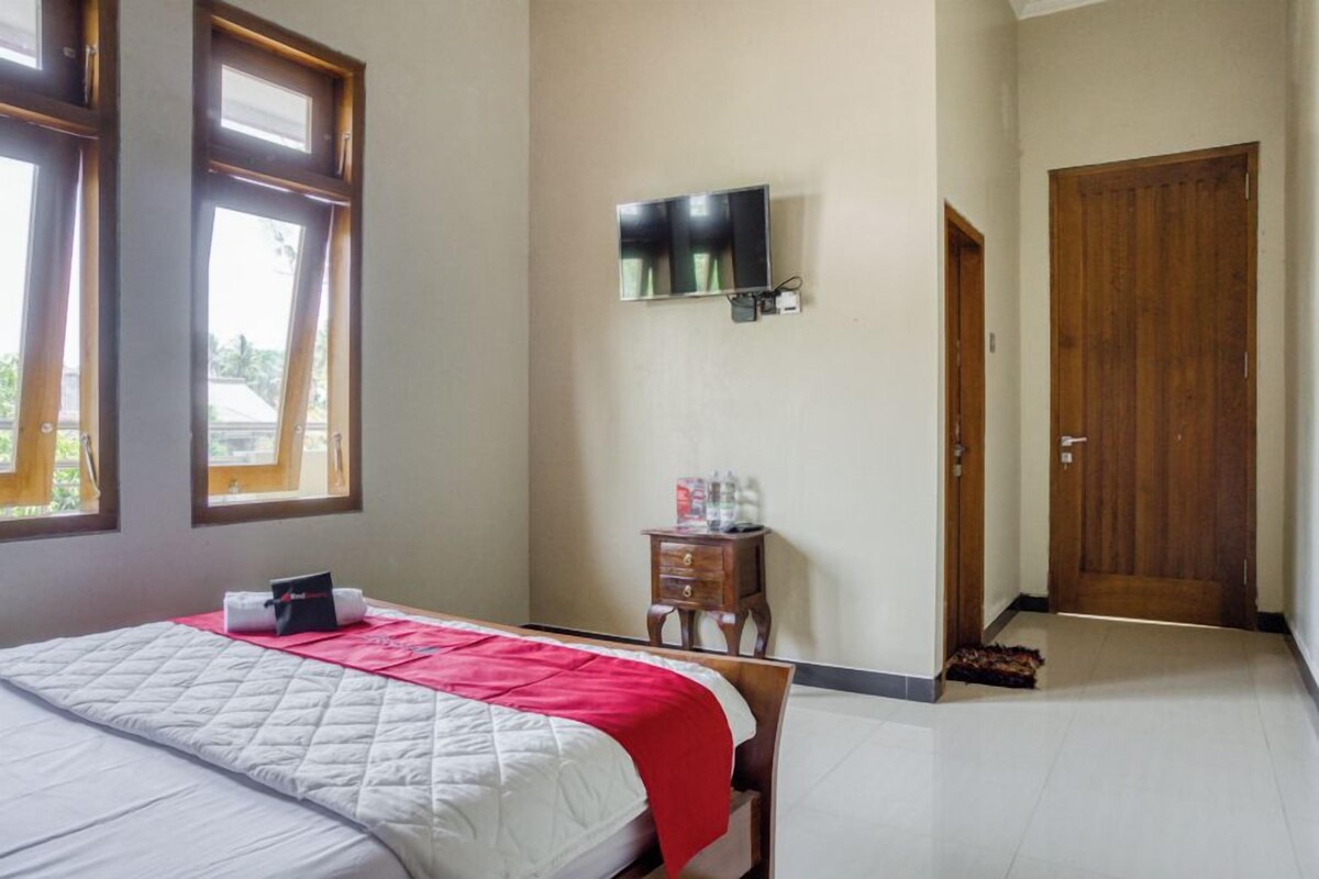 Quarto de hotel com cama, televisão fixada na parede, porta de madeira e janela com persianas.