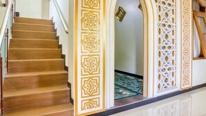 Una escalera con escalones de madera y barandilla blanca que conduce a una habitación con piso estampado y paneles decorativos en la pared.