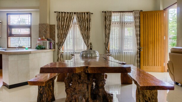 Una habitación amplia con una gran mesa de comedor de madera, un banco y una zona de cocina con ventana y cortinas.