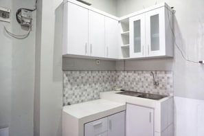 A kitchen with white cabinets, a tiled backsplash, and a stainless steel sink. - Reddoorz Syariah @ Berlian Homestay Wirobrajan (Yogyakarta)