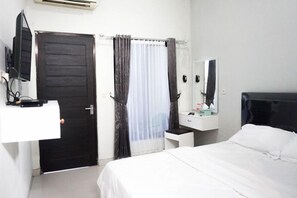 A hotel room with a bed, a desk with a mirror, a wardrobe, and a door. - Reddoorz Syariah @ Berlian Homestay Wirobrajan (Yogyakarta)
