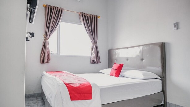 Una cama bien hecha con una colcha blanca y roja, un cabecero gris y una ventana con cortinas.