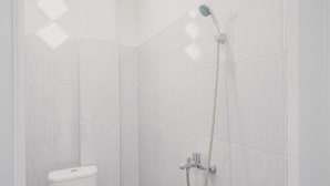 Un baño con azulejos blancos, inodoro y ducha con cabezal de ducha manual.