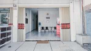 Entrada de un hotel con piso de baldosas, un mostrador de recepción y una sala de espera con sillas.