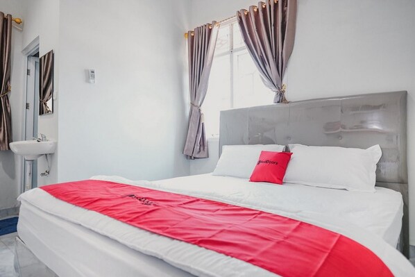Une chambre d’hôtel avec un grand lit, une table de chevet, un miroir, une fenêtre avec des rideaux et une salle de bain équipée d’un lavabo et d’un miroir.